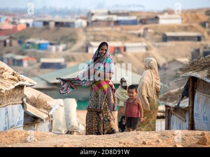 Rohingya people walk around as shelters are seen behind them at Kutupalong refugee camp in Maynar Guna, near Cox's Bazar, Bangladesh on April 16, 2018. Rohingya people, who fled from oppression in Myanmar, try to live in hard conditions at makeshift settlements made from bamboo, adobe or nylon at Kutupalong refugee camp.  Over 650,000 Rohingya have crossed the border to Bangladesh since August last year, fleeing the violence. Stock Photo