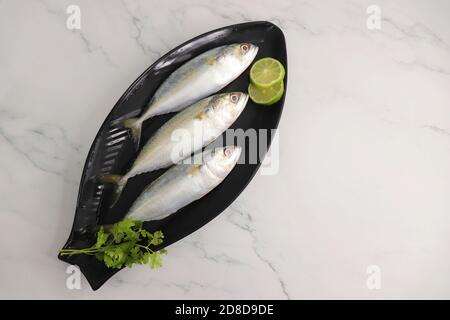 Uncooked Indian mackerel fish Rastrelliger kanagurta. also known as Bangda fish. Free copy space. Lemon wedge and coriander. top view fish background. Stock Photo