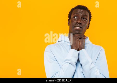 Image of concentrated african american guy in streetwear hoodie looking upward at copyspace isolated over yellow background Stock Photo