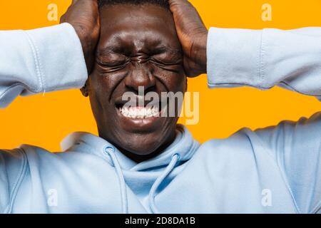 Image of tense african american guy in streetwear hoodie suffering and grabbing his head isolated over yellow background Stock Photo
