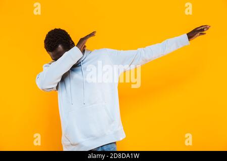Image of young african american guy in streetwear hoodie making dab arms gesture isolated over yellow background Stock Photo