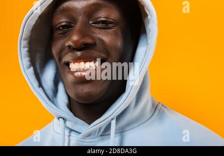 Image of happy african american guy wearing hood smiling and looking at camera isolated over yellow background Stock Photo