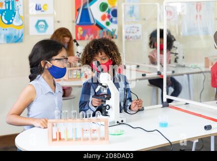 Boy and girl wearing face mask using microscope in laboratory Stock Photo