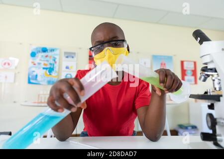 Boy wearing face mask and protective glasses mixing chemicals in laboratory Stock Photo