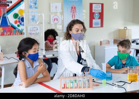 Female teacher wearing face mask and protective glasses teaching students in laboratory Stock Photo