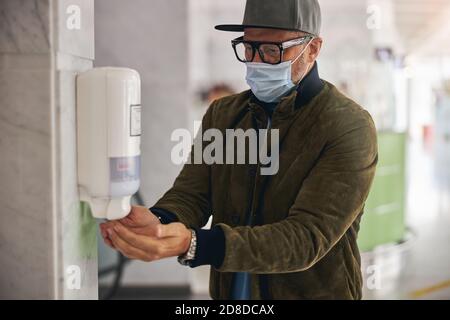 Tourist in eyeglasses disinfecting his hands in a public place Stock Photo