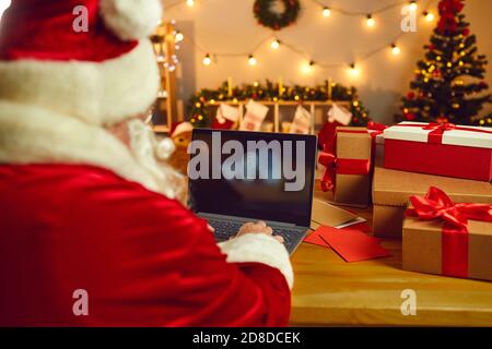View from the back of Santa Claus sitting at a table and turning on a laptop for work. Stock Photo