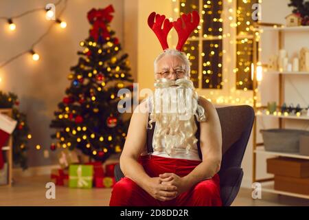 Serious Santa Claus wearing reindeer antlers relaxing in armchair after long day of work Stock Photo