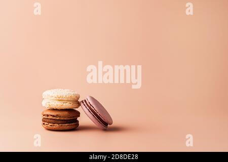 Three macaroons chocolate, vanilla and berry in stack on pastel background for your design. Food concept in vintage style. Copy space. Closeup. Stock Photo