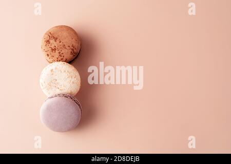 Three macaroons chocolate, vanilla and berry on pastel background for your design. Food concept in vintage style. Copy space. Closeup. Flat lay style. Stock Photo