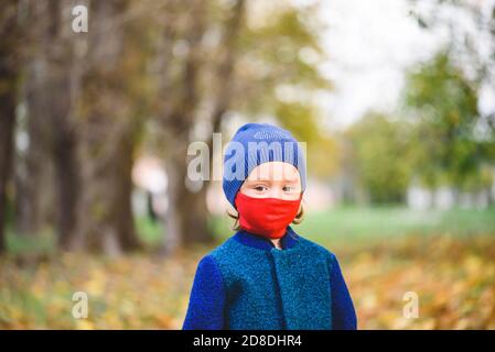 Concept of new normal with little girl in red protective face mask and warm clothes walking in autumn park Stock Photo