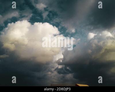 Dramatic massive dark clouds under blue sky settle for heavy rainfall in day time Stock Photo