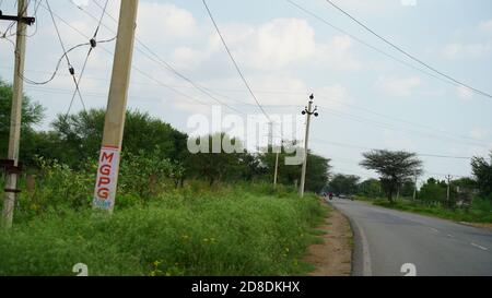 22 September 2020 : Mahroli, Rajasthan, India / Village road and electricity pole. Indian rural landscape. View of empty Red Road in the morning with Stock Photo