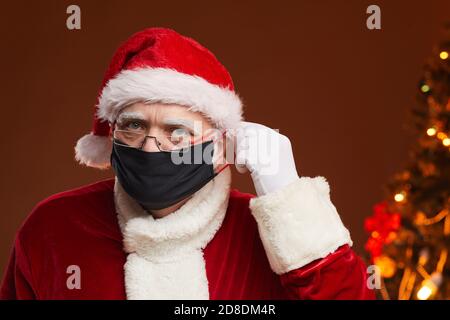 Portrait of senior man in red costume wearing protective mask celebrating Christmas in pandemic Stock Photo