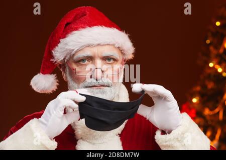 Portrait of senior bearded man in Santa costume wearing protective mask he protecting himself in pandemic Stock Photo