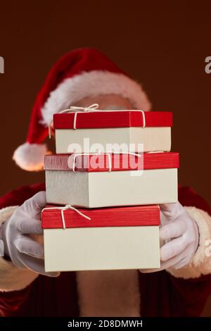 Portrait of Santa Claus holding stack of gift boxes in front of his face against the brown background Stock Photo