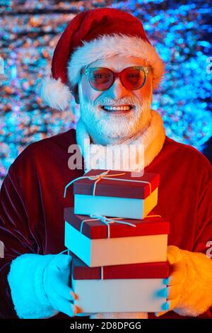 Happy Santa Claus in sunglasses holding gift boxes and smiling at camera Stock Photo