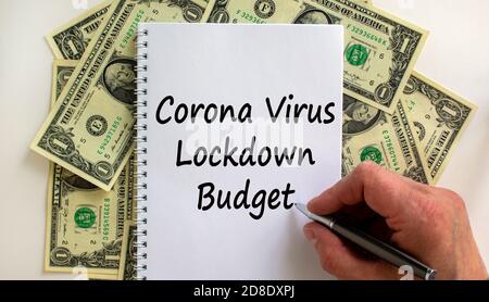 Male hand writing 'corona virus lockdown budget' on white note, on white background. Dollar bills. Stock Photo
