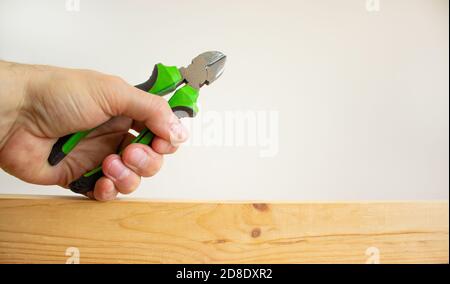A male hand holds a wire cutters on a wooden bar. Beautiful white background. Copy space. Concept. Stock Photo