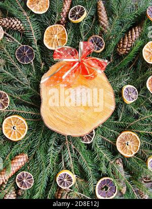 Wooden slice on green fir-tree branches decorated with dried orange slices and cones. Christmas and New Year vintage winter holiday festive compositio Stock Photo