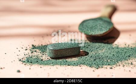 Close-up of chlorella or spirulina tablets and wooden spoon with powder among powder on pink background in the sun Nutritional supplement, detox Stock Photo