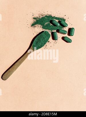 Close-up of chlorella or spirulina tablets and a wooden spoon with powder on a light pink background in sun. Nutritional supplement, detox superfood Stock Photo