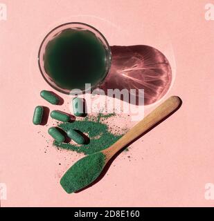 Drink, tablet and spoon with chlorella or spirulina powder on a pink background in the sun. Nutritional supplement, detox superfood Stock Photo