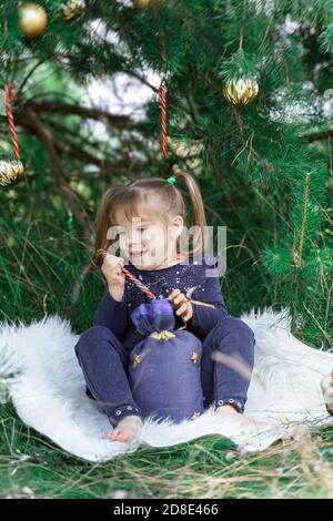 child girl takes Christmas caramel out of a gift bag. christmas tree in the forest. christmas without snow Stock Photo