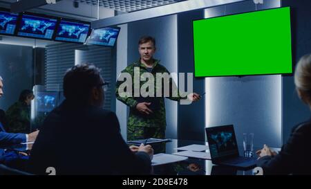 High-Ranking Military Man holds a Briefing to a Team of Government Agents and Politicians, Points at Green Mock-up Screen Wall TV. Stock Photo