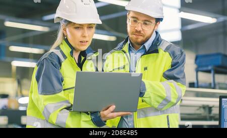 Inside the Manufacturing Factory Male Mechanical Engineer Works on Personal Computer Under Supervision of Female Chief Project Engineer. Stock Photo
