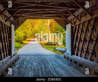 looking from the inside of historic Comstock covered bridge out at road covered in fall foliage colored trees Stock Photo