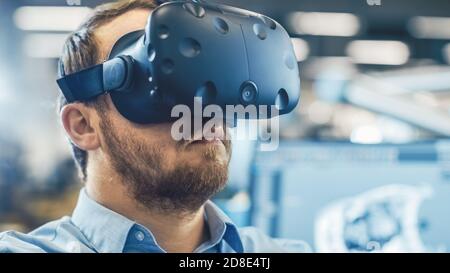 Portrait Shot of the Industrial Engineer Wearing Virtual Reality Headset and Gesturing with Controllers. In the Background Out of Focus Displays and Stock Photo