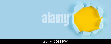 Ripped Paper Hole with yellow coloured background. Torn hole in blue paper, ripped edges. Long wide banner. Copy space for your design. Stock Photo