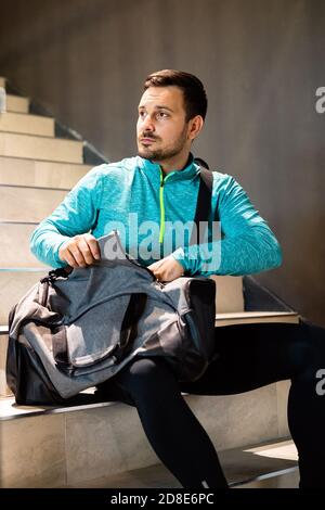 Portrait of young fit man athlete with bag after workout in gym