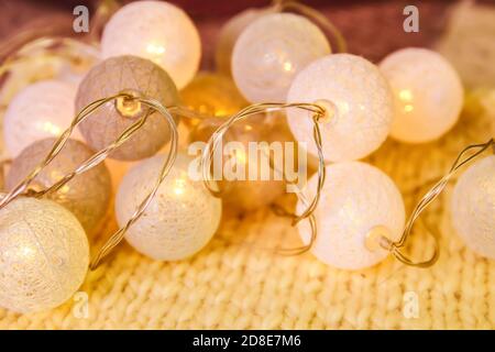 Christmas lights garland with round lanterns on knitted fabric background. Stock Photo