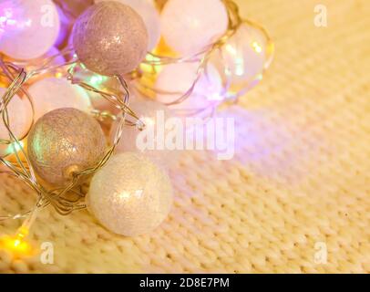 Christmas lights garland with round lanterns on knitted fabric background. Stock Photo