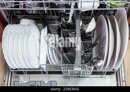 Opened dishwasher with clean plates, spoons is in the kitchen, close up view Stock Photo