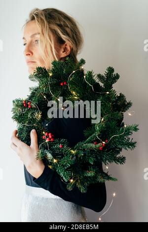 A young elegant woman holds a decorated Christmas wreath on her shoulder. Stock Photo