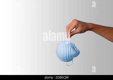 Hand of a Latino man holding a medical mask is about to drop it on white background. End of confinement. Copy Space. Stock Photo