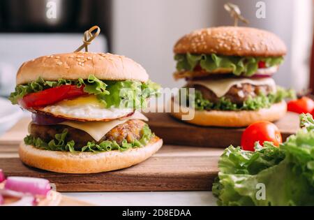 Two home made fresh tasty burgers with lettuce and cheese. Ingredients on the table. Light food background. Stock Photo
