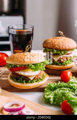 Two home made fresh tasty burgers with lettuce and cheese. Ingredients on the table. Light food background. Stock Photo