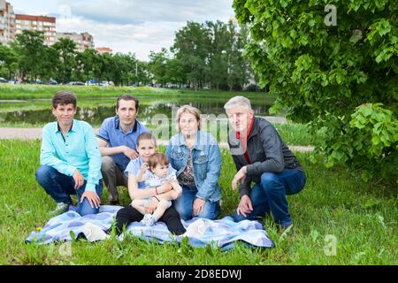 Six people family portrait at weekend picnic, senior grandparents, adult single father, preteen age girl and boy, toddler girl sitting on blanket on a Stock Photo