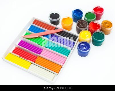 Cardboard box with colorful plasticine bars, plastic knife and color paints in bottles, a white background Stock Photo