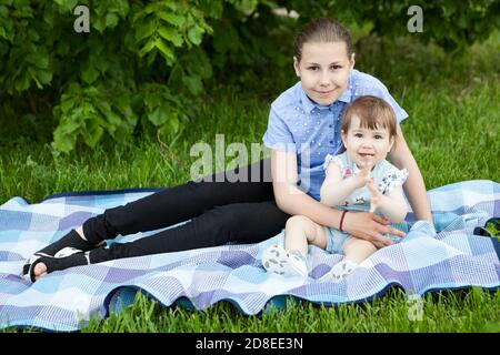 Happy and smiling sisters of teen and infant ages are on weekend picnic in a summer park Stock Photo