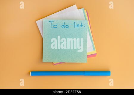 Square note sheet with the inscription to do list. Multi-colored notes on a yellow background and a blue felt-tip pen. top view. Stock Photo