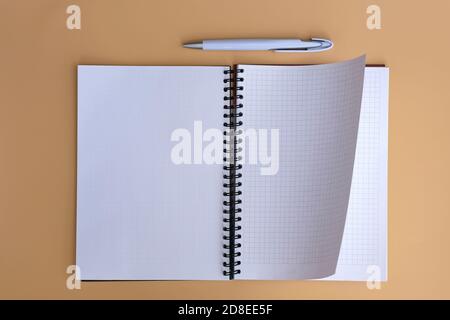 Spring notepad, checkered sheets  top view. Checkered notebook with a flip sheet on a beige background with a pen. Opened notebook with white sheets. Stock Photo