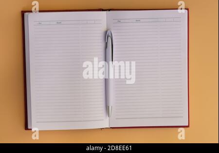 Notepad with horizontal lines on a yellow background top view. Notebook with white pen. Blank sheets of notebook. Diary with a red cover for the to-do Stock Photo