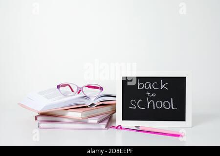 Open book, pile of books in pink and purple covers, glasses, pen, pencil, ruler abd blackboard frame on white background Stock Photo