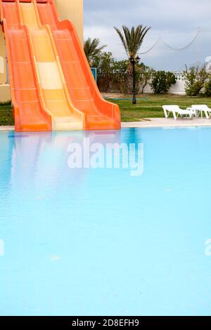 Closed water slides are in waterpark in a hotel, calm water surface of a swimming pool, empty resort area Stock Photo