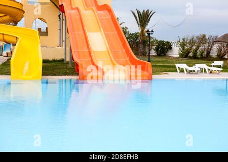 Closed water slides are in aquapark, calm water surface of swimming pool, an empty resort area Stock Photo